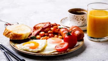A plate with eggs, bacon, sausages, beans, and a tomato, accompanied by toast and a glass of orange juice.