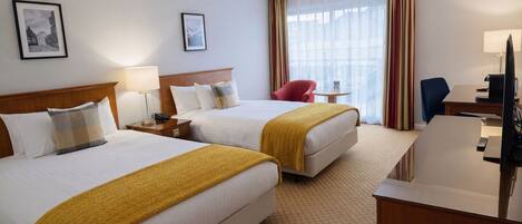 A hotel room with two beds, a desk, a chair, a TV, and a window with curtains.
