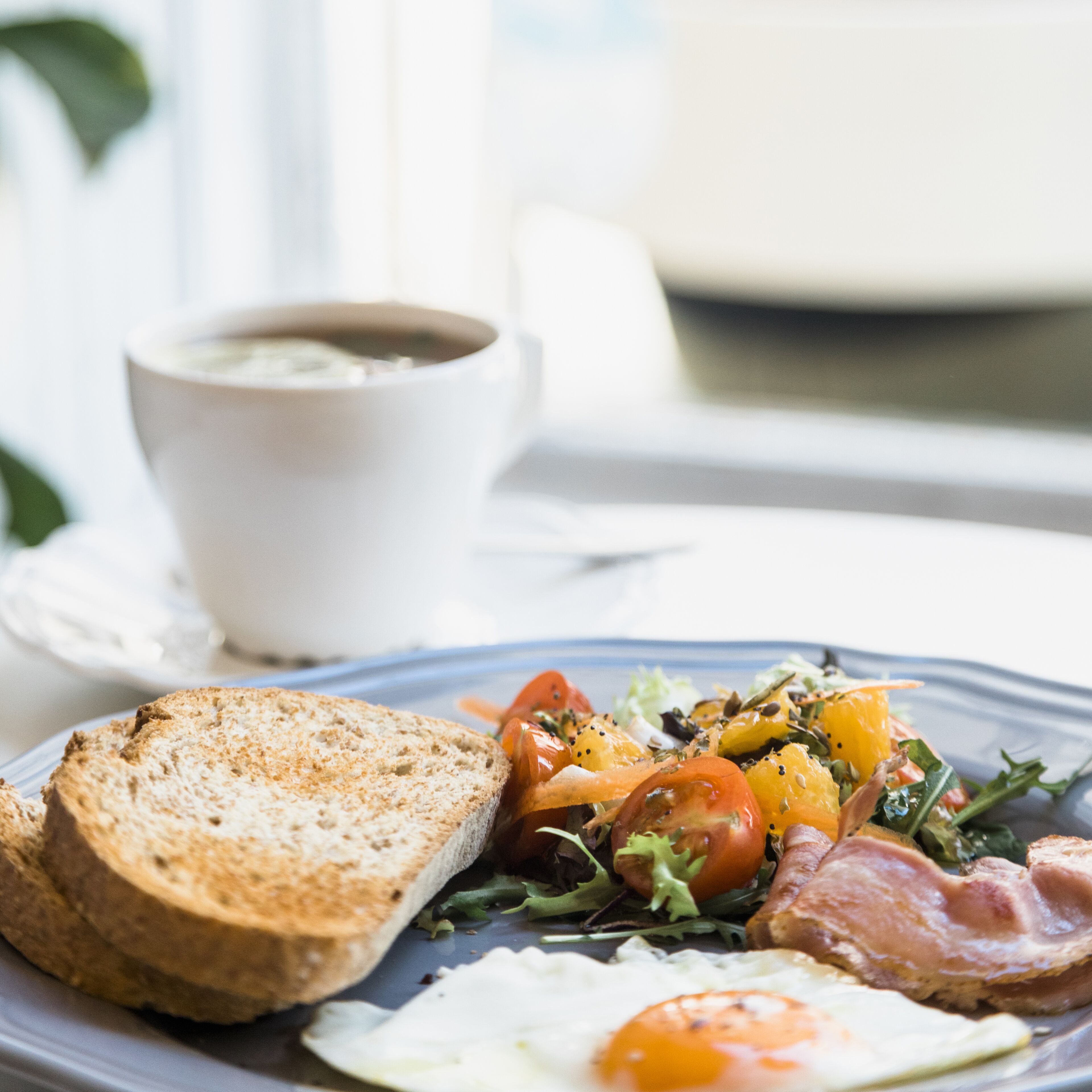 A breakfast plate with toast, eggs, tomatoes, and greens, and a cup of coffee on a table.