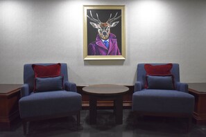 A room with two blue armchairs, a small round table, and a framed painting of a deer in a suit on the wall. - The Aberdeen Dyce Hotel (Aberdeen)