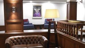A lobby with a leather armchair, a wooden bench, a blue sofa, and a painting of a deer in a suit. - The Aberdeen Dyce Hotel (Aberdeen)