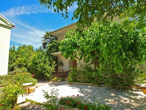 Une cour avec un bâtiment blanc, entourée d’une végétation luxuriante et de diverses espèces de plantes.