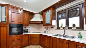 A kitchen with wooden cabinets, a built-in oven, a sink, and a window with potted plants. - Holiday apartment with air conditioning (Rovinj)