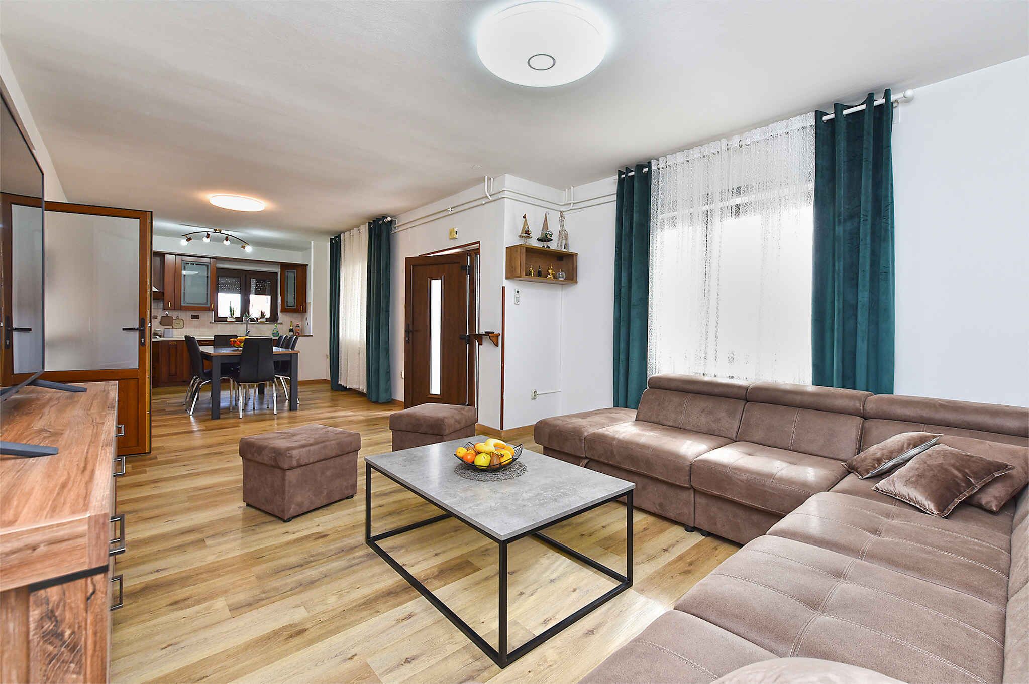 A modern living room with a brown leather sofa, a wooden dining table, and a kitchen in the background.