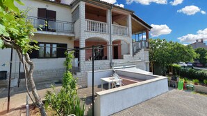 A two-story house with a balcony, a small patio area with a table and chairs, and a garden with plants and a tree. - Holiday apartment with air conditioning (Rovinj)