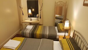Camera d'albergo con due letti, ognuno con lenzuola a righe e una lampada. C'è una scrivania con uno specchio e una finestra con tende.