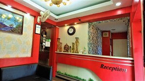 Un espace d’accueil avec un mur rouge, un tableau encadré, une horloge et un comptoir d’accueil.