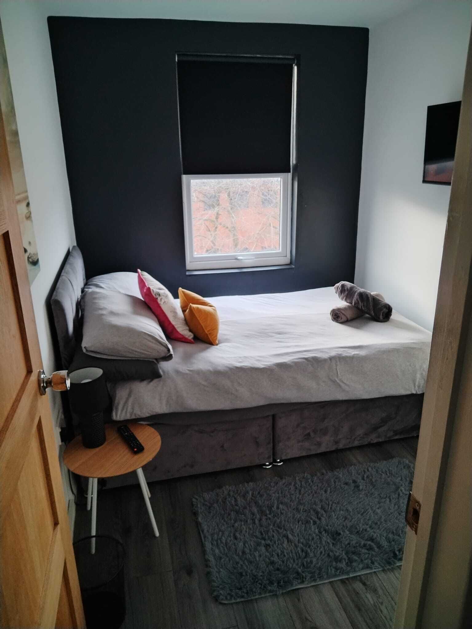Un dormitorio pequeño y funcional con una cama individual, una ventana y una mesita con un control remoto.