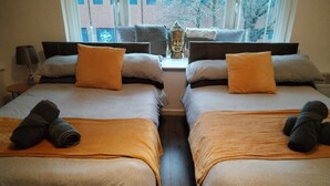 Une chambre d’hôtel avec deux lits, chacun recouvert d’une couverture marron et agrémenté d’une serviette enroulée. Une fenêtre offre une vue sur les bâtiments et les arbres à l’extérieur.