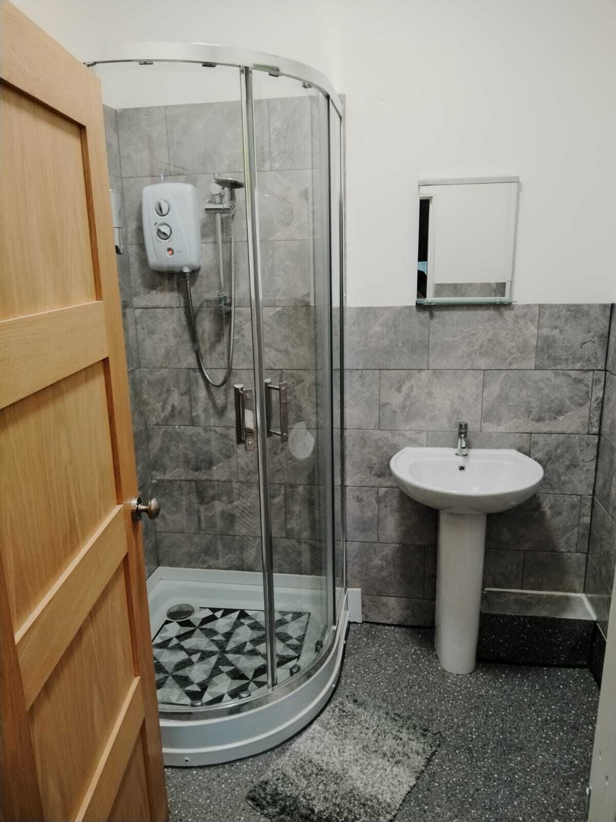 Een badkamer met een douchecabine van glas, een wastafel op een voetstuk en een vloer met een patroon.