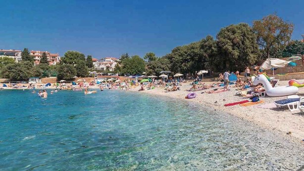 Une plage avec une eau claire, des parasols et des gens.