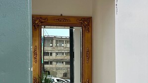 A corner room with a large ornate mirror, a small shelf with a vase, and a view of a building through the window. - 1 bedroom apartment in ercolano (Ercolano)