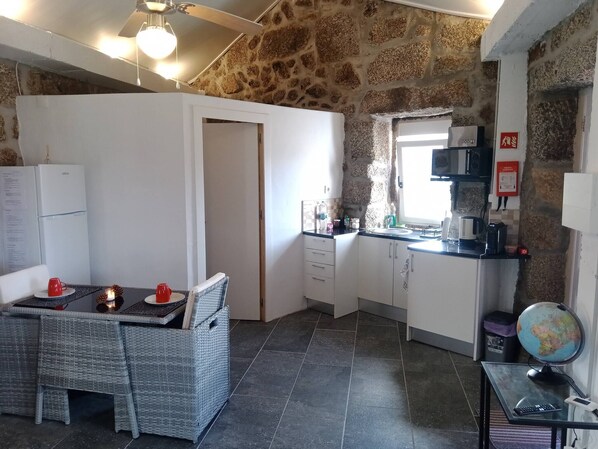 A compact kitchen with a stone wall, a dining area with wicker furniture, and a small table with candles.