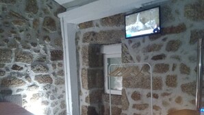 Ein Schlafzimmer mit einer Steinstur, einem Bett, einem an der Wand montierten Fernseher und einem Fenster mit Vorhang.