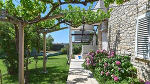 A stone building with a stone wall and a wooden pergola with vines. - Holiday apartment with air conditioning (Medulin)