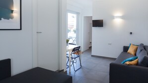 Een moderne woonkamer met een bank, een eethoek met stoelen en een aan de muur bevestigde televisie.