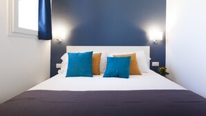 Een netjes opgemaakt bed met een wit hoofdeinde, blauwe en bruine kussens en een donkerblauwe deken.