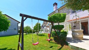 A residential setting with a swing set, a stone building, and a well-maintained lawn. - Holiday apartment with air conditioning (Medulin)