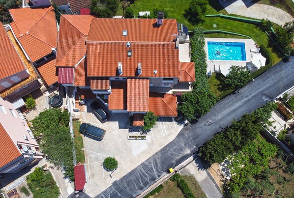 Vue aérienne d’un quartier résidentiel avec une piscine, une maison au toit rouge et une grande allée.
