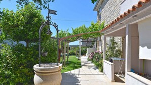 A pathway leading to a house with a stone planter, a metal gate, and a pergola with a red beam. - Holiday apartment with air conditioning (Medulin)