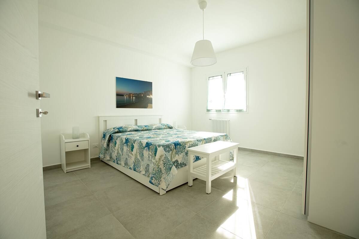 Ein Schlafzimmer mit einem Bett, einem Nachttisch, einem Fenster und einem Bild an der Wand.