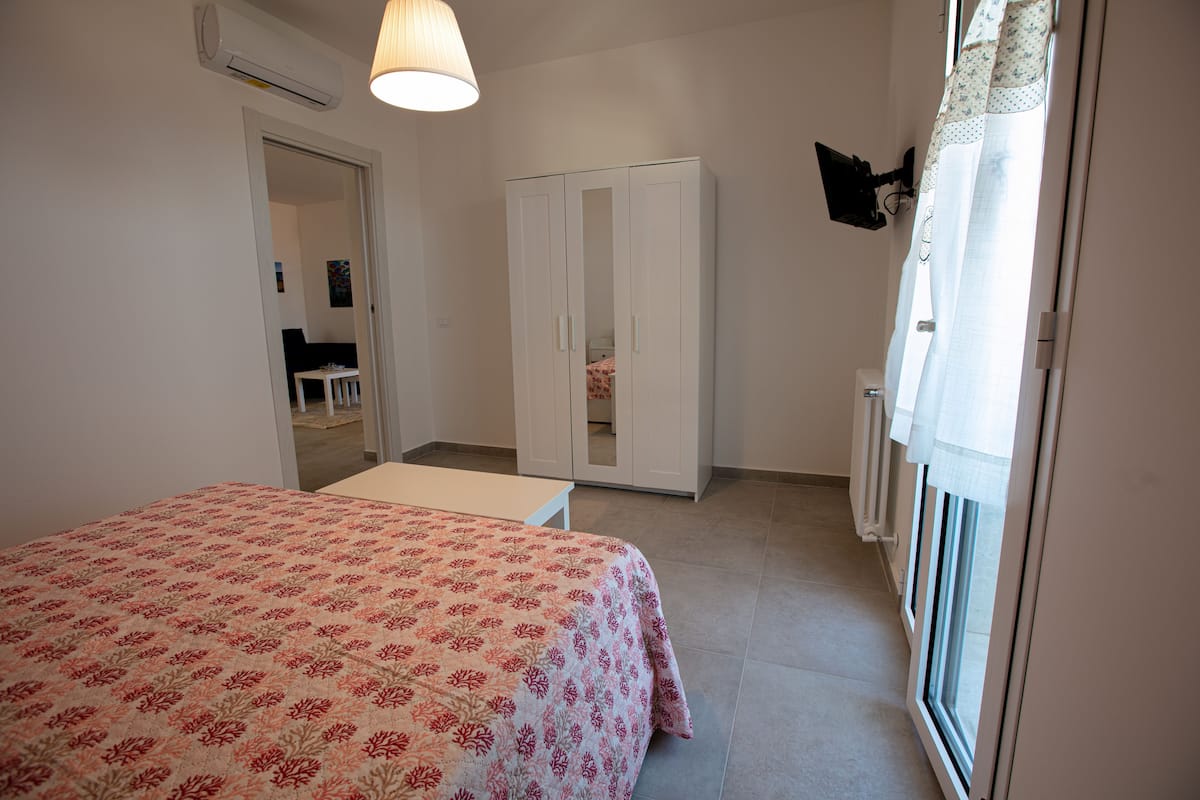 Ein Schlafzimmer mit Bett, Kleiderschrank, Schreibtisch und einem Fenster mit Vorhängen.