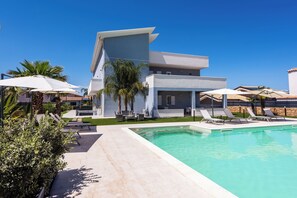 A modern poolside area with lounge chairs and umbrellas, a clear blue sky, and a contemporary building with balconies. - Etna Mare Apartments by Wonderful Italy (Augusta)