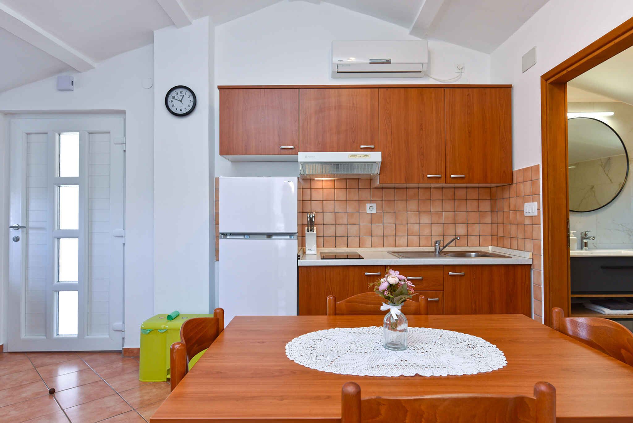 A kitchen with wooden cabinets, a white refrigerator, and a sink. There's a dining table with chairs and a vase with flowers.