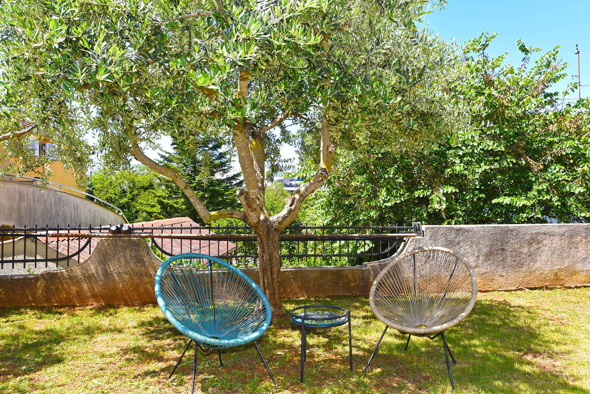 A tree-lined outdoor seating area with two wicker chairs and a small table.