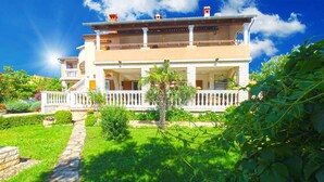 A two-story building with a balcony, a stone pathway, and lush greenery. - Holiday apartment with air conditioning (Medulin)