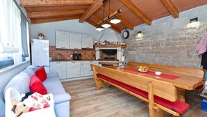 Eine gemütliche Küche mit Holztisch und Bank, einer Couch mit roten Kissen und einer Steinwand.