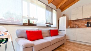 Eine moderne Küche mit Holzboden, einem grauen Sofa und roten Kissen sowie einem Fenster mit Jalousien.