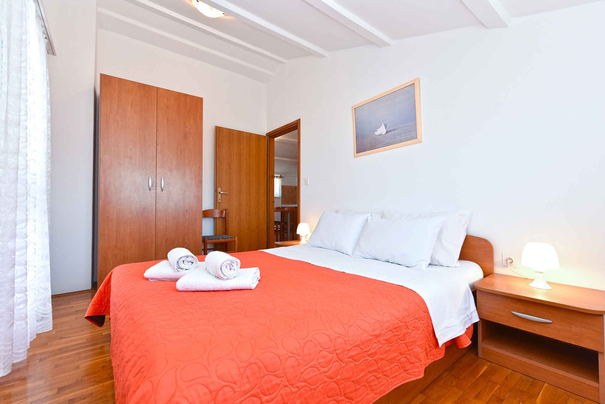 A bedroom with a bed, a wooden wardrobe, a nightstand, and a framed picture on the wall.