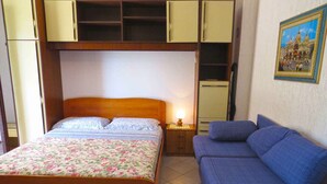 A bedroom with a bed, a nightstand, a dresser, a sofa, and a painting on the wall.