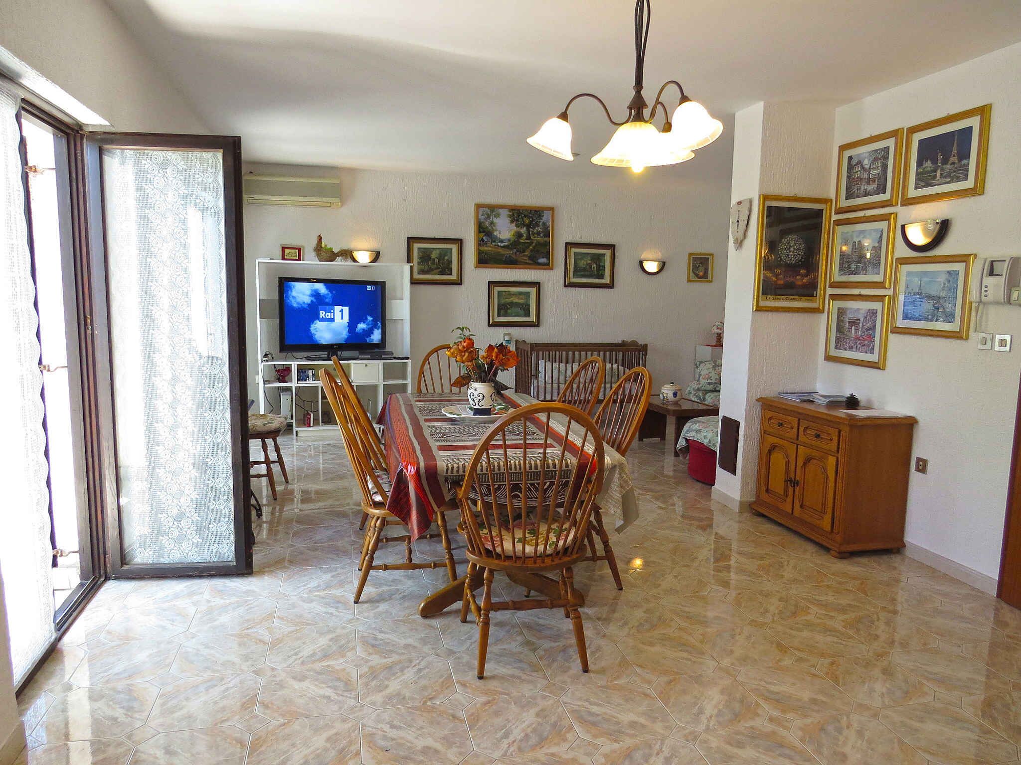 Uma área de refeições com televisão, mesa, cadeiras e um armário.