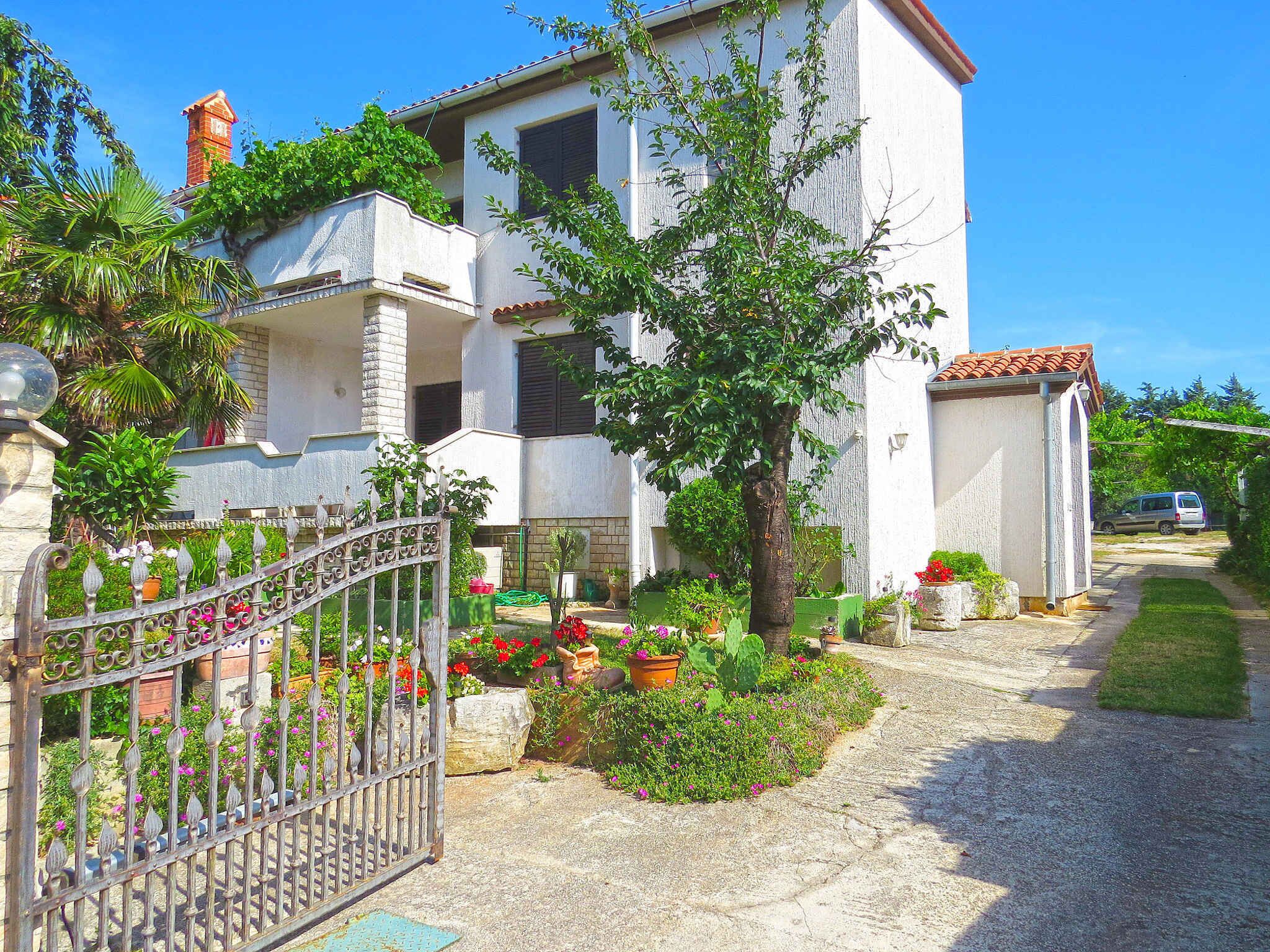 A two-story house with a garden in front, a metal gate, and a car parked outside.