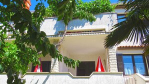 A two-story building with a balcony, a stone wall, and a palm tree in the foreground. - Holiday apartment with air conditioning (Medulin)