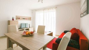A modern living room with a wooden dining table, a red sofa, and a TV on a stand.