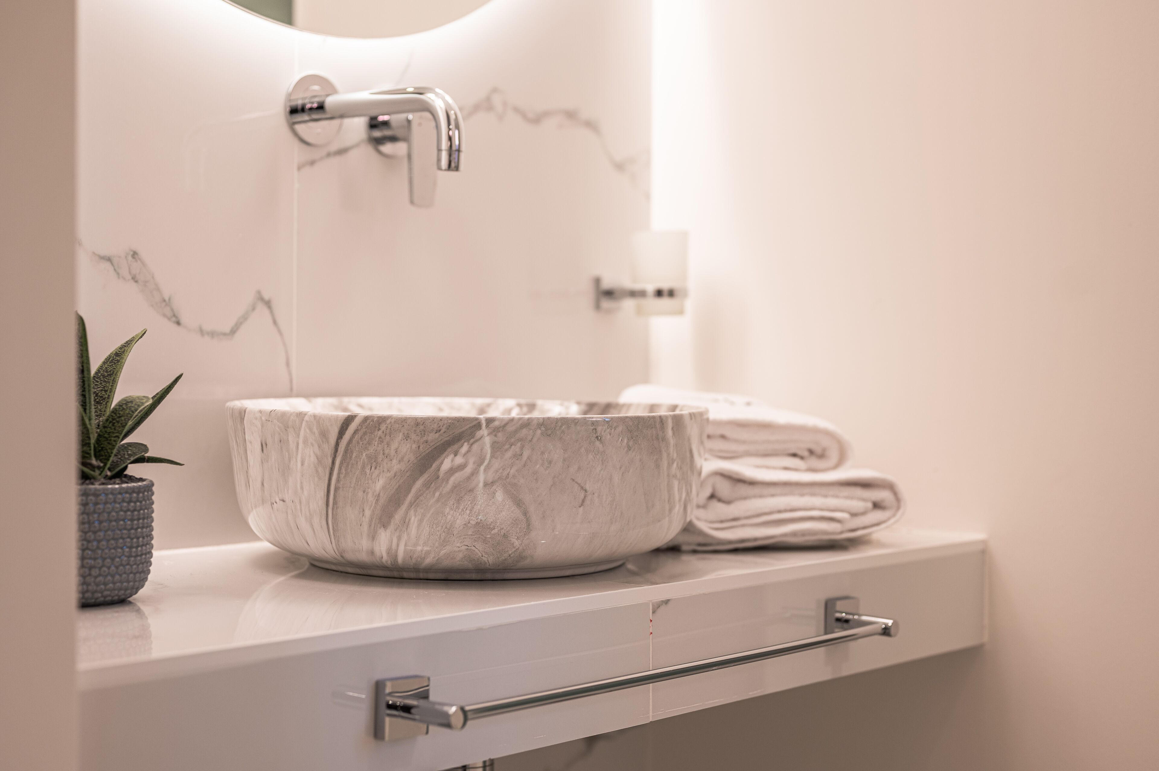 Un baño con lavamanos de mármol, toallero e planta en maceta.