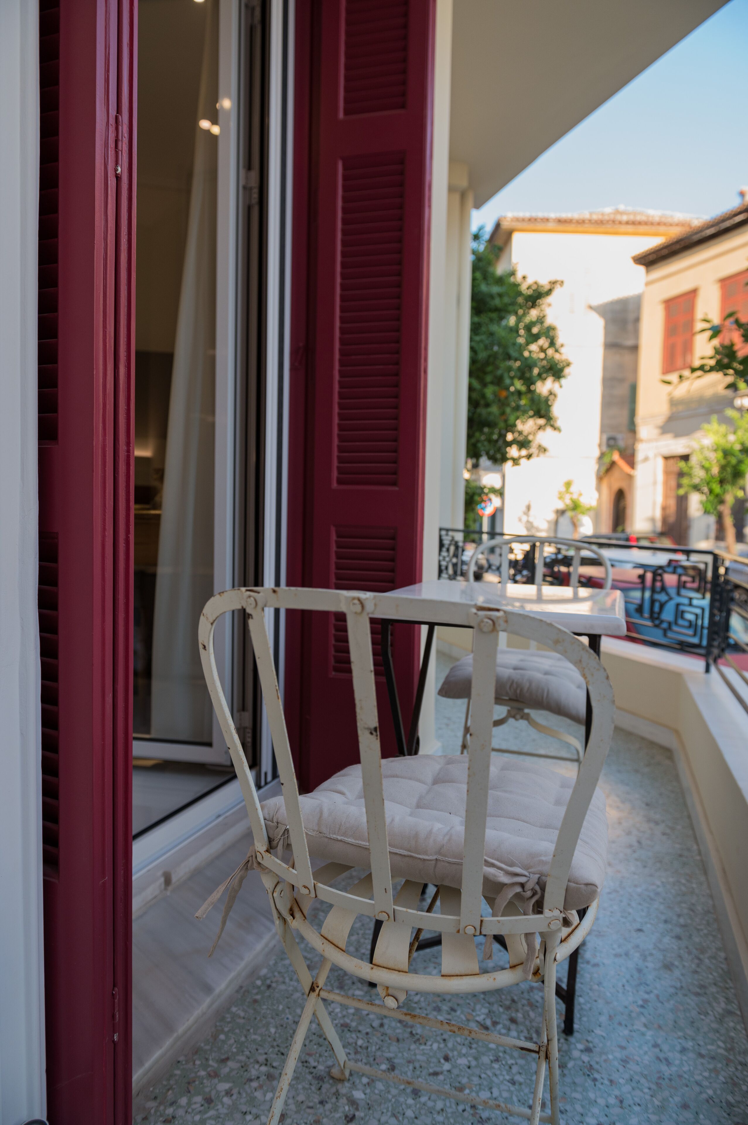 A white wicker chair with a cushion on a balcony with red shutters.