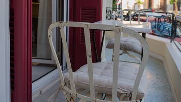A white wicker chair with a cushion on a balcony with red shutters.