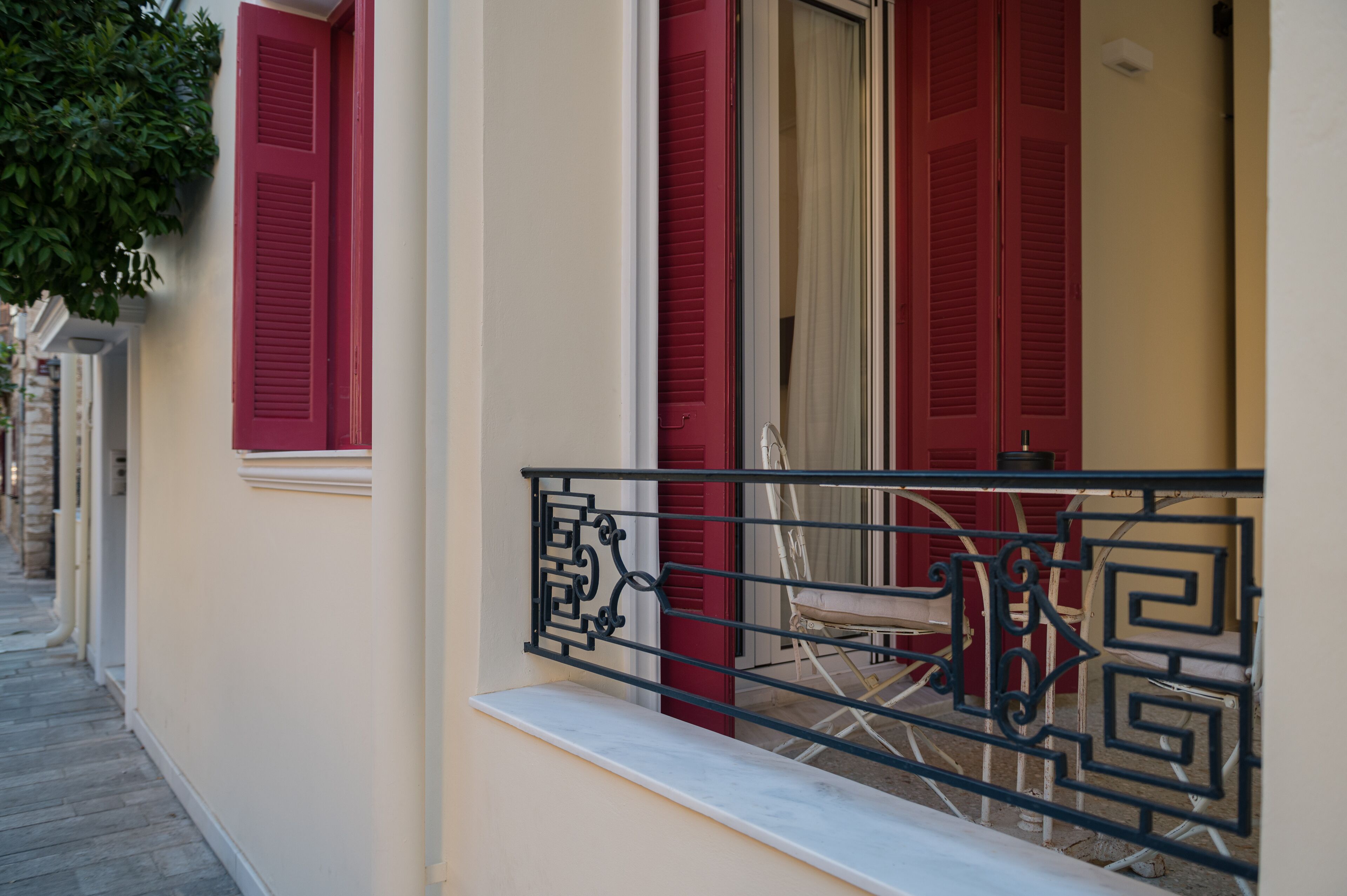 A building with red shutters, a white balcony with a metal railing, and a chair.