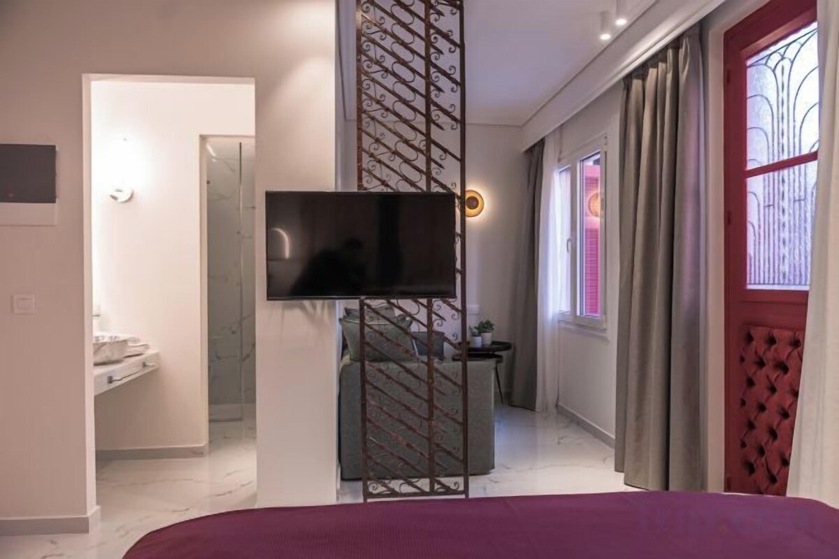 Een moderne hotelkamer met een bed, een televisie, een badkamer met een wastafel en een raam met gordijnen.