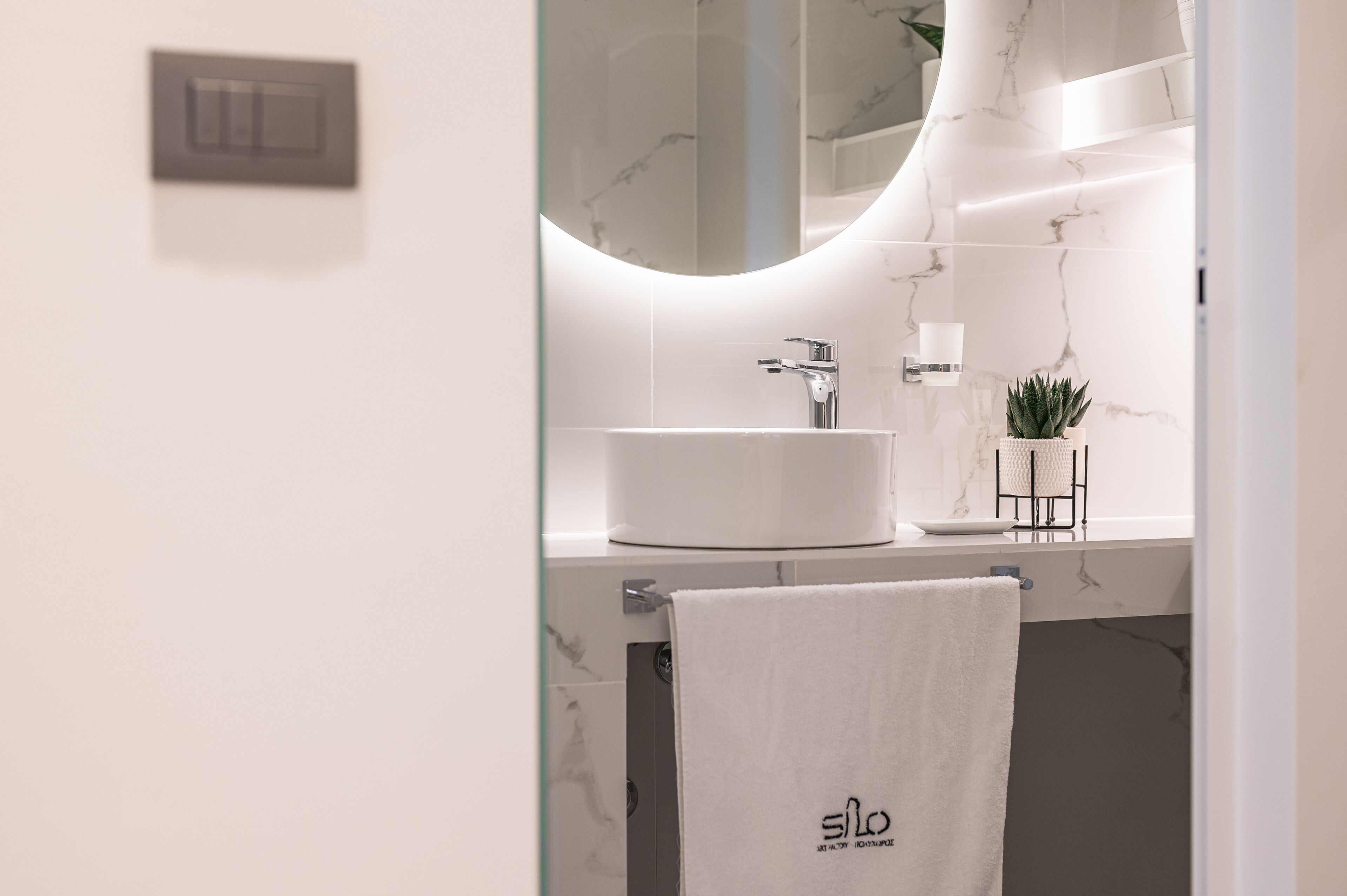 A modern bathroom with a white marble sink, a mirror, and a towel rack.