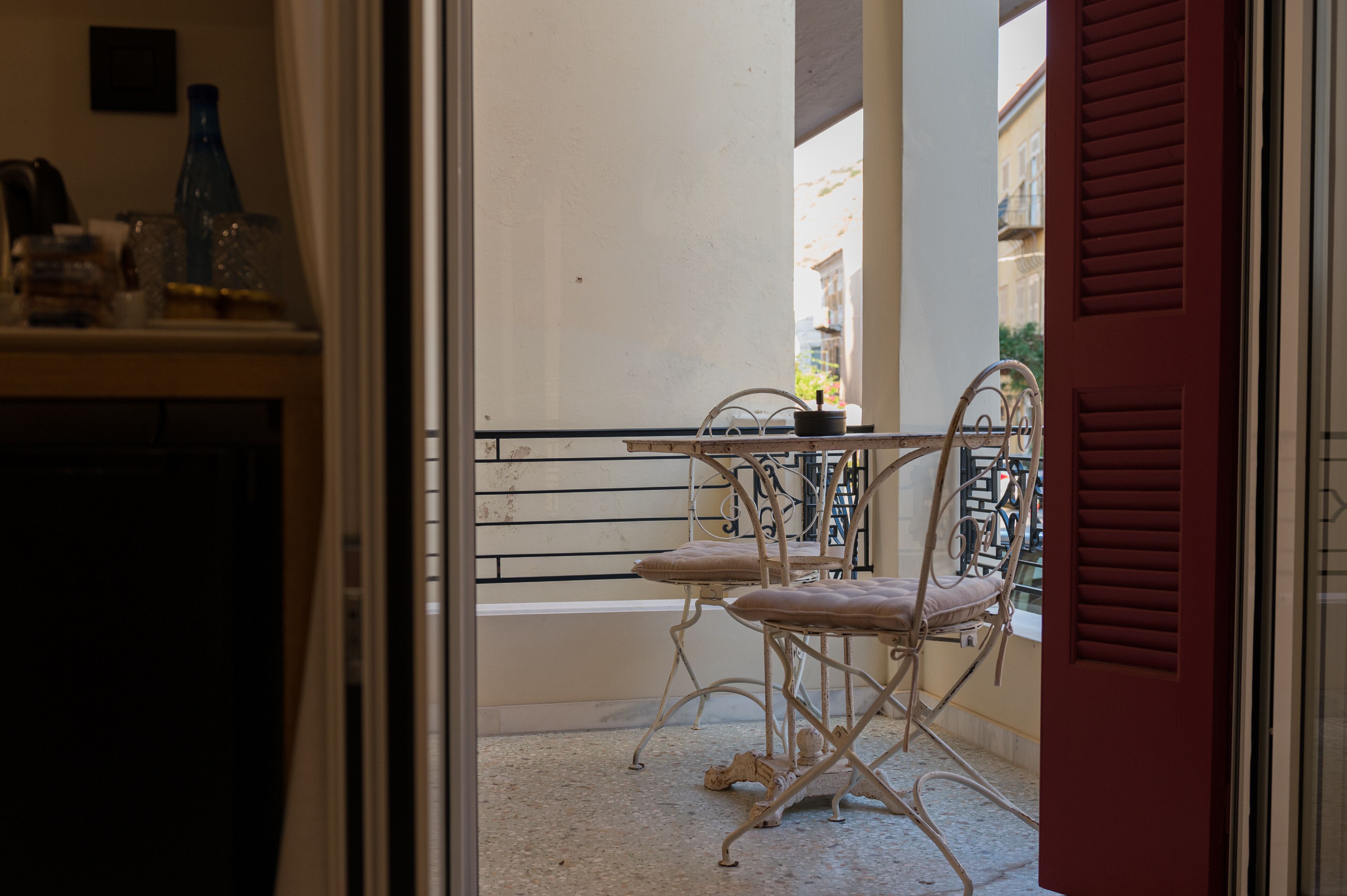 A balcony with a table and two chairs, a bottle, and a vase on the windowsill.