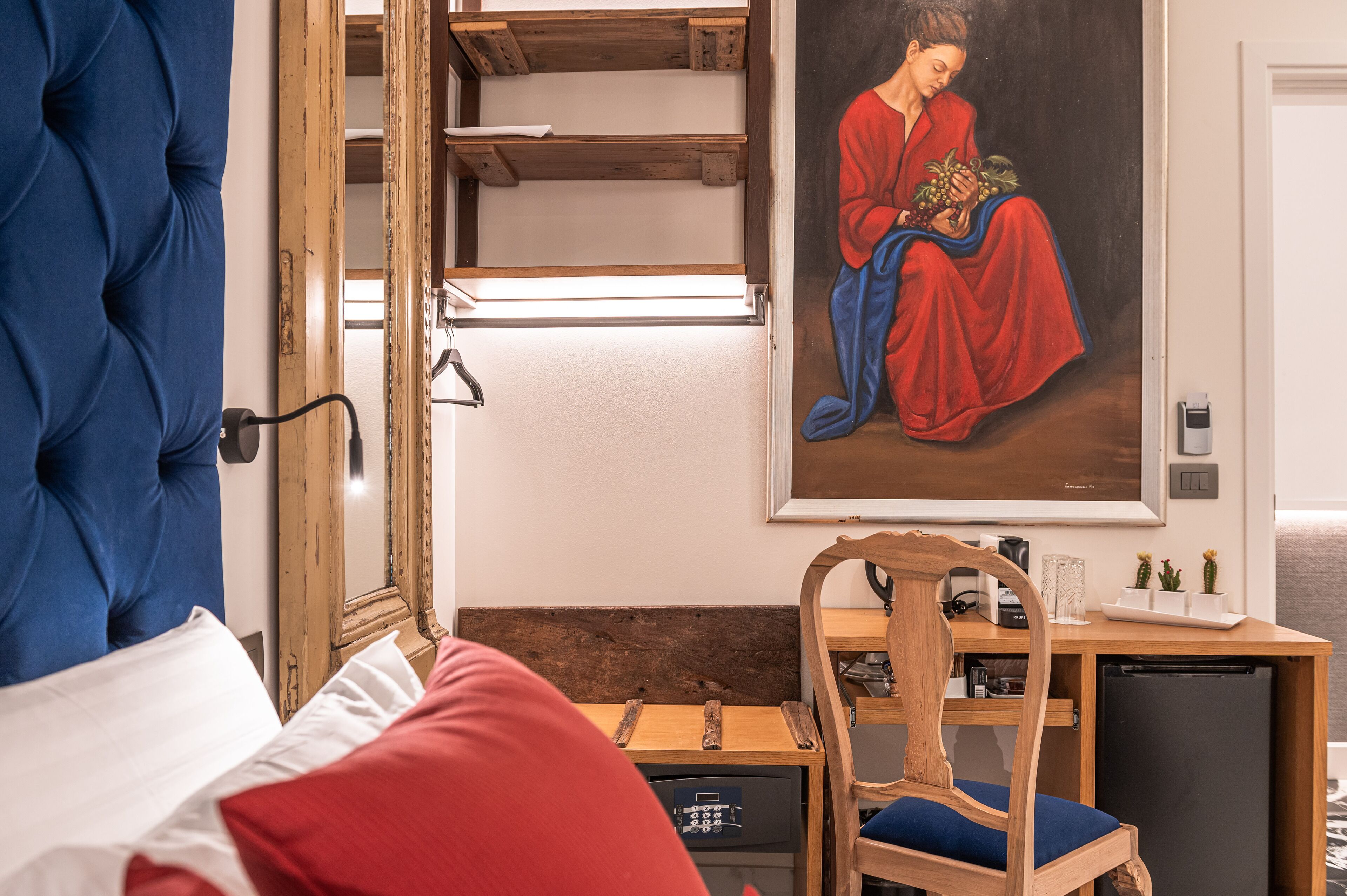 Een slaapkamer met een groot bed, een houten bureau, een stoel, een kleine koelkast en een schilderij aan de muur.