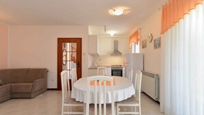 A living room with a beige sofa, a dining table with white chairs, a kitchen area with a stove, and a radiator. - Holiday apartment with air conditioning (Medulin)