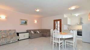 A living room with a sofa, a dining table with chairs, a kitchen area, and a small cabinet. - Holiday apartment with air conditioning (Medulin)