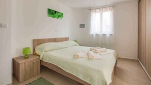 A bedroom with a bed, a nightstand, a green lamp, and a window with curtains.