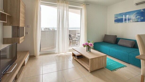 Ein modernes Wohnzimmer mit Fernseher, Couchtisch aus Holz, einem smaragdgrünen Sofa und einem Balkon mit Gartenmöbeln.